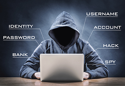 A man in a hoodie engaging in cybercrime at a table with a laptop.