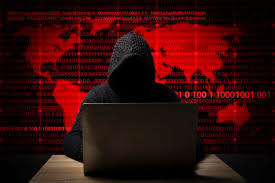 A man engaged in cybercrime wearing a hoodie is sitting at a desk with a laptop.